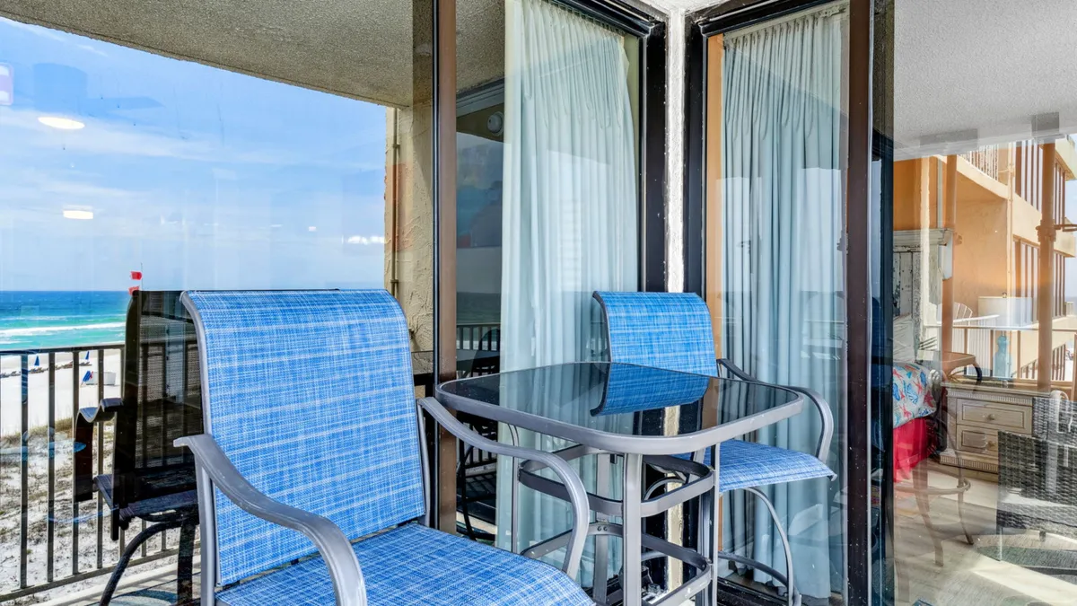 An outdoor balcony furnished with blue patio chairs and a glass table, offering an unobstructed view of the ocean. The setting is tranquil—ideal for sipping morning coffee or enjoying an evening toast as the sun sets over the Gulf.
