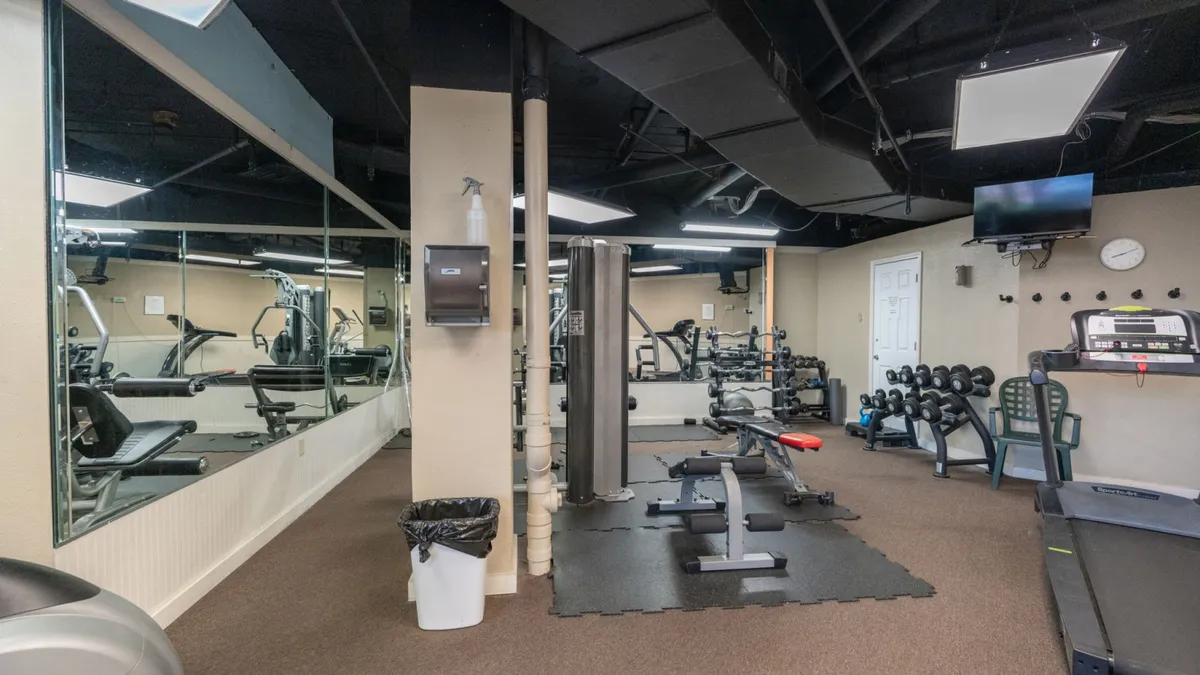 An energetic fitness center with a treadmill, weight bench, free weights, exercise machines, and a mirrored wall. The space is well-lit and inviting, designed for personal workouts or group fitness sessions, supporting an active lifestyle.
