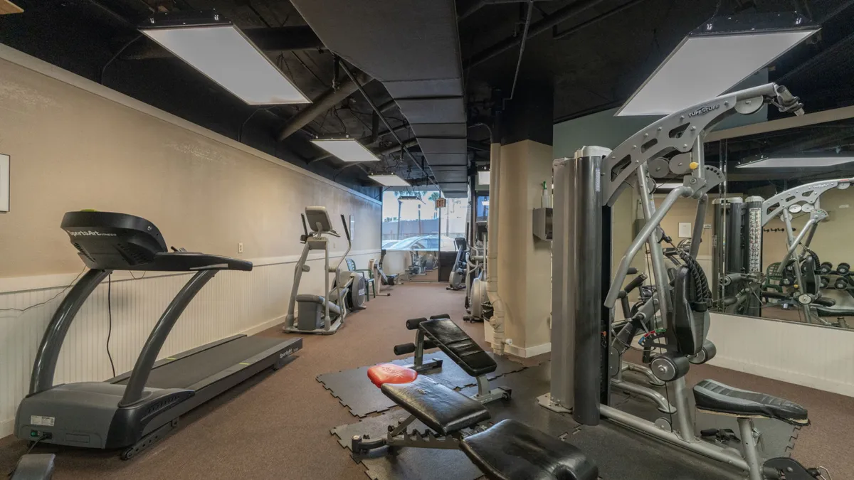 An interior scene of a modern fitness center filled with treadmills, weight benches, and exercise machines. Large mirrors amplify the space, and the mood is energetic, with a focus on both individual and group workouts.