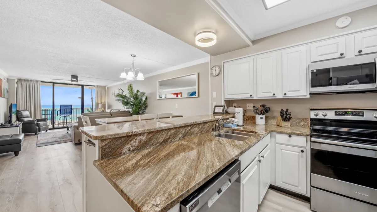This image features a modern kitchen with a granite countertop and stainless steel appliances. A panoramic window offers beautiful views, bringing in natural light and a coastal feel. The kitchen appears spacious and inviting, ideal for cooking and entertaining.