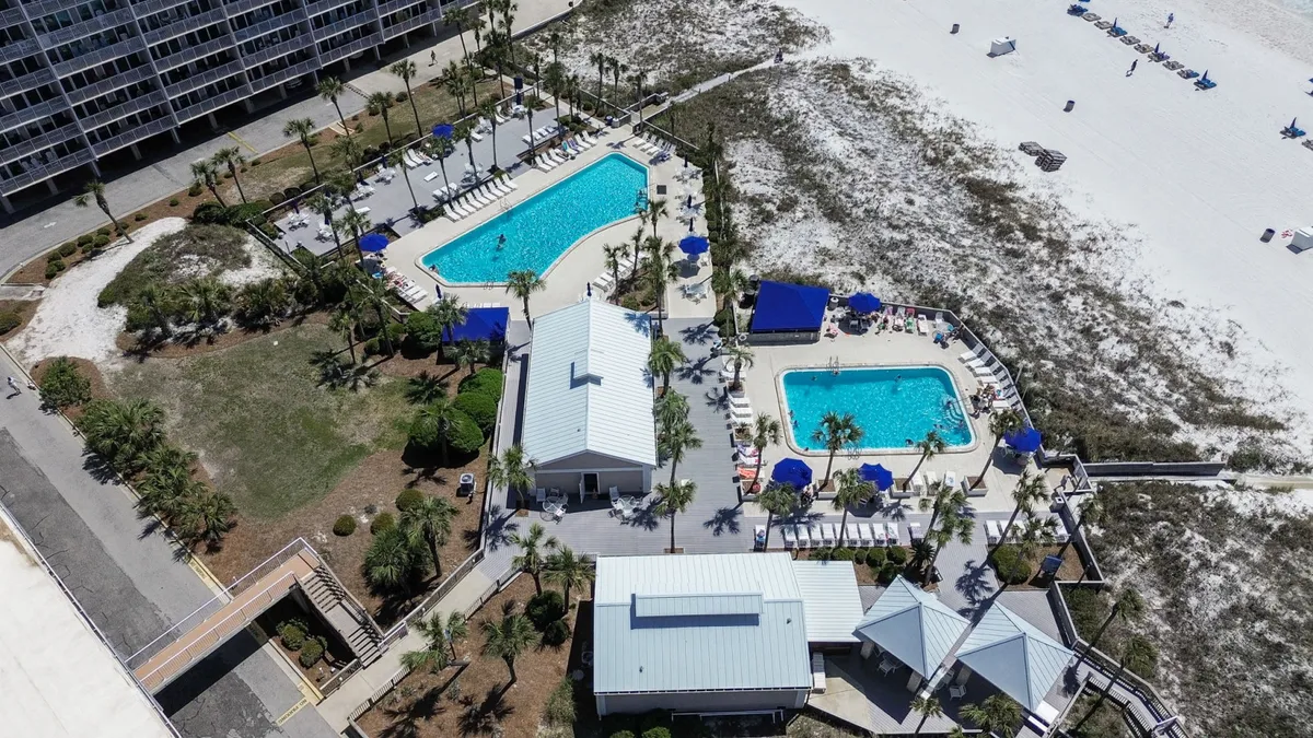 An exterior view of two sparkling swimming pools surrounded by swaying palm trees and inviting lounge areas. The pools are large and family-friendly, with open spaces for play, relaxation, and social gatherings, capturing the vibrant resort atmosphere.