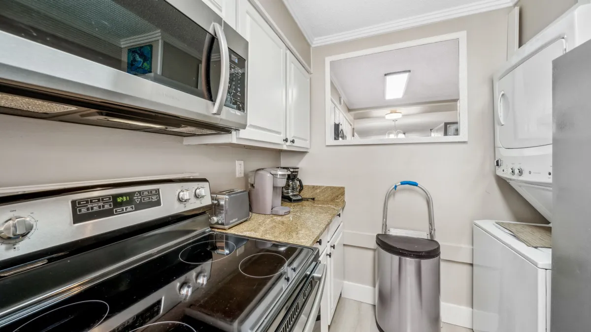 A detailed view of the kitchen’s functional amenities, including a stainless steel electric stove, overhead microwave, granite countertop with coffee maker and toaster, and a stacked washer and dryer unit tucked neatly into the space.
