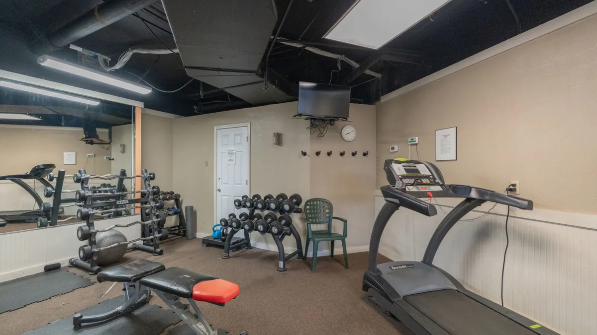 A modern fitness center featuring a treadmill, dumbbell racks, a weight bench, and a wall-mounted TV. The equipment is arranged neatly in a bright, inviting indoor space, reflecting a clean and motivating environment for workouts.